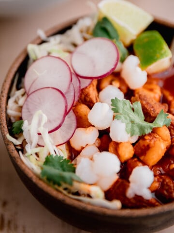 Pork Pozole Roja in a bowl topped with radish, cilantro and lime.