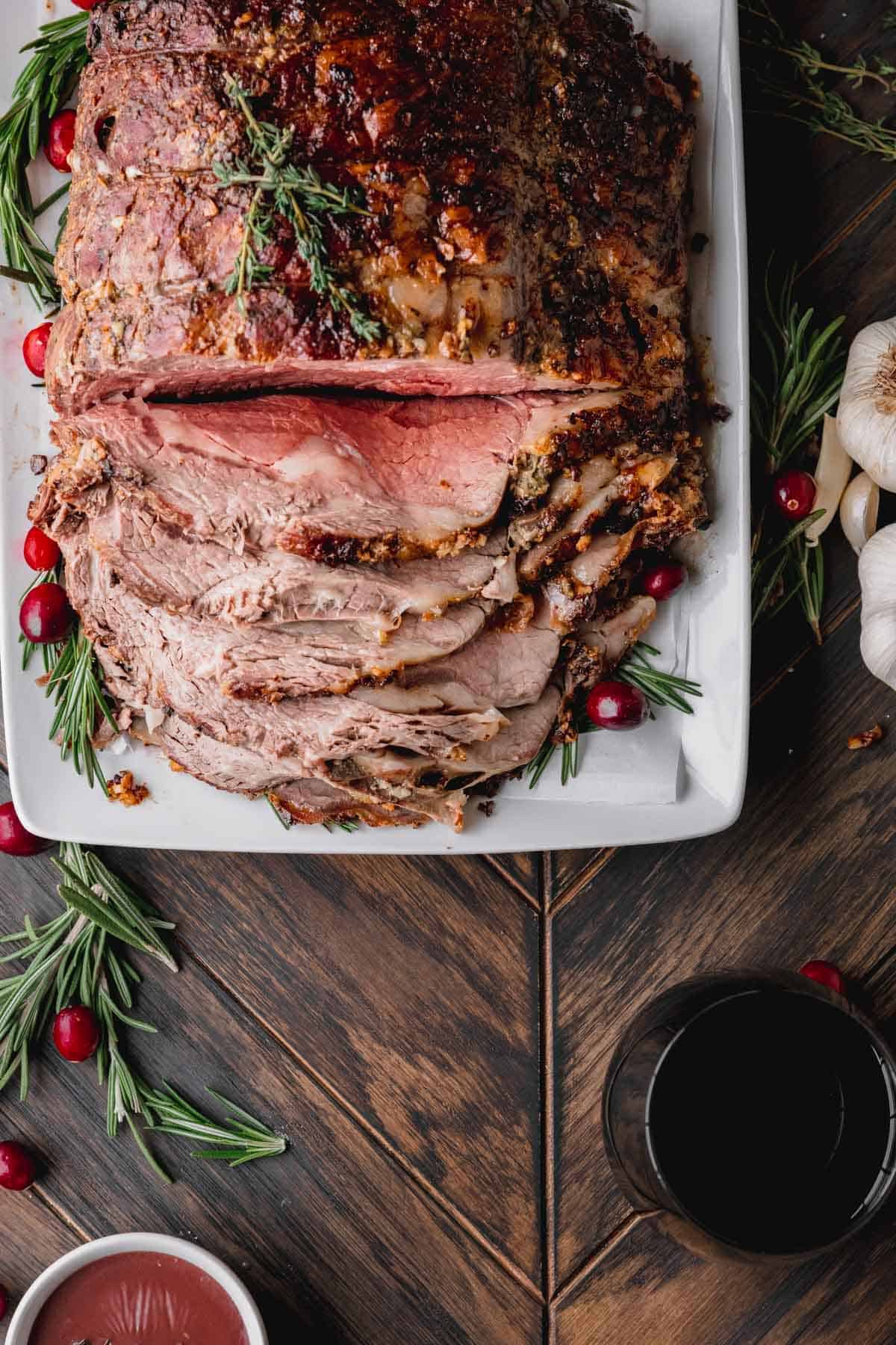 Standing Rib Roast partially sliced on a platter with fresh rosemary and cranberries. 