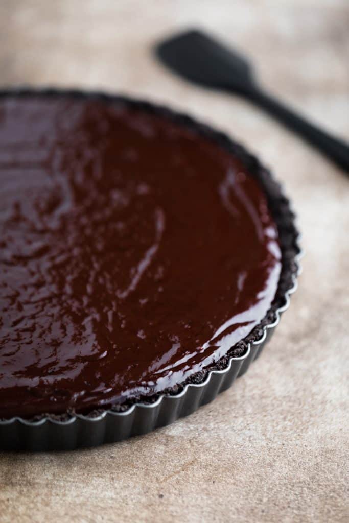 chocolate ganache tart in the tart pan with a rubber spatula laying next to it