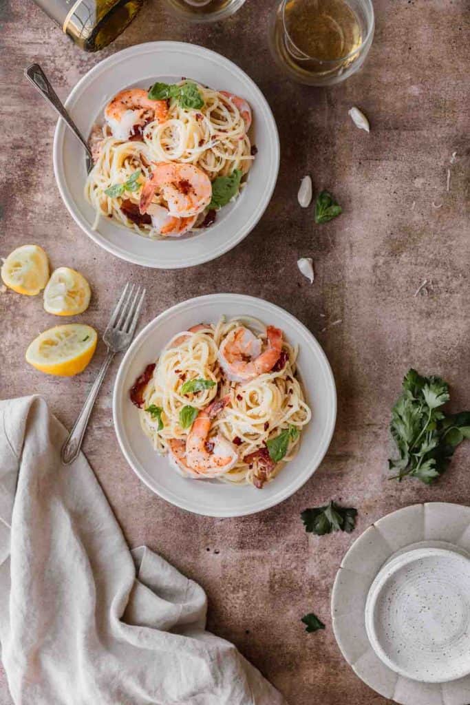 shrimp and pasta with lemon and crispy prosciutto in bowls with squeezed lemons to the side