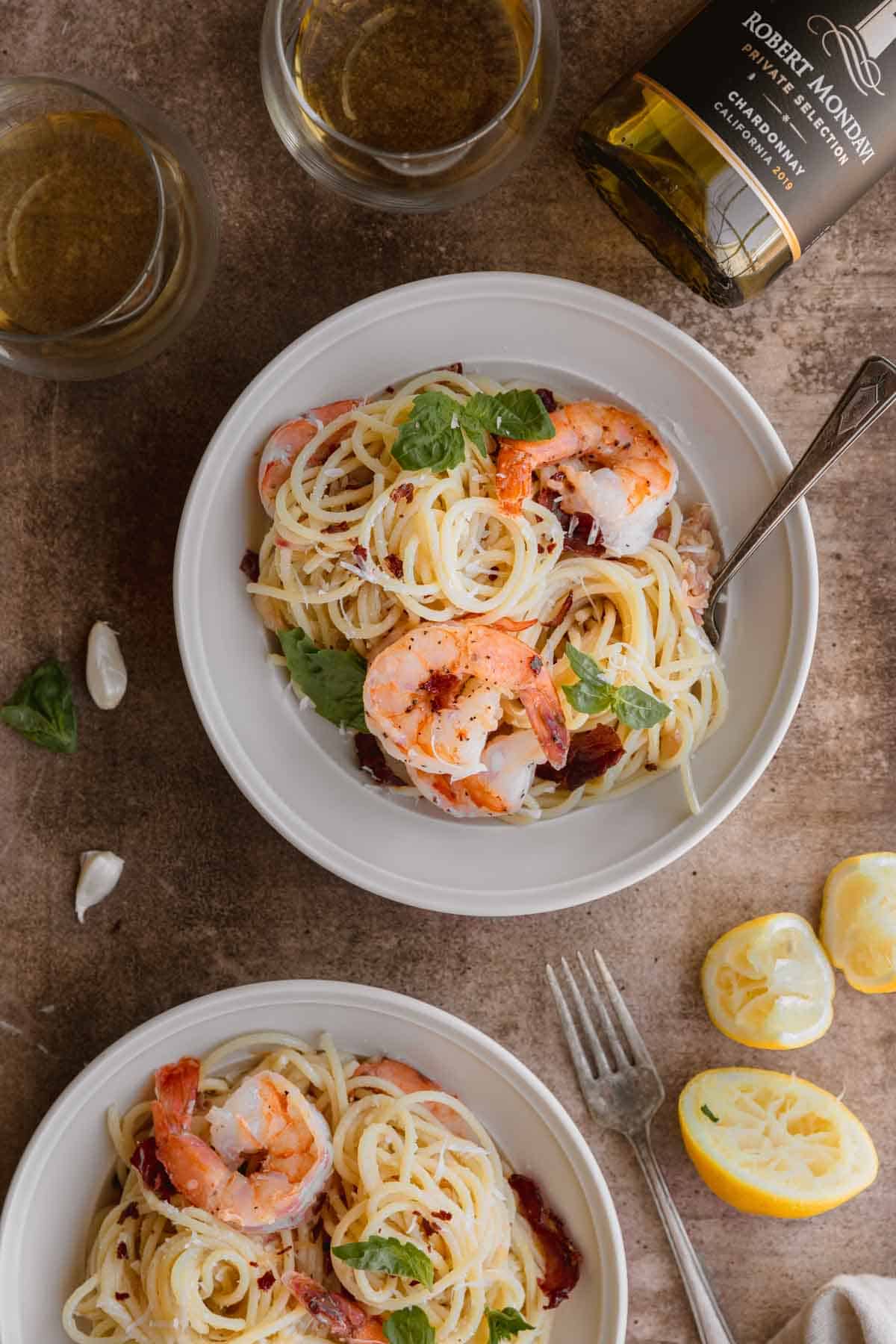 Shrimp pasta with lemon and crispy prosciutto in a bowl with lemon wedges on the side. 