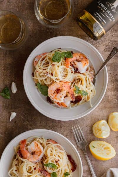 shrimp and lemon pasta with crispy prosciutto in a bowl with a wine bottle and glass of wine above it