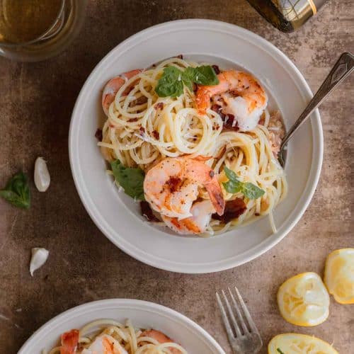 shrimp and lemon pasta with crispy prosciutto in a bowl with a wine bottle and glass of wine above it
