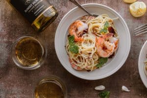 shrimp and lemon pasta with crispy prosciutto in a bowl with a glass of wine and wine bottle next to it