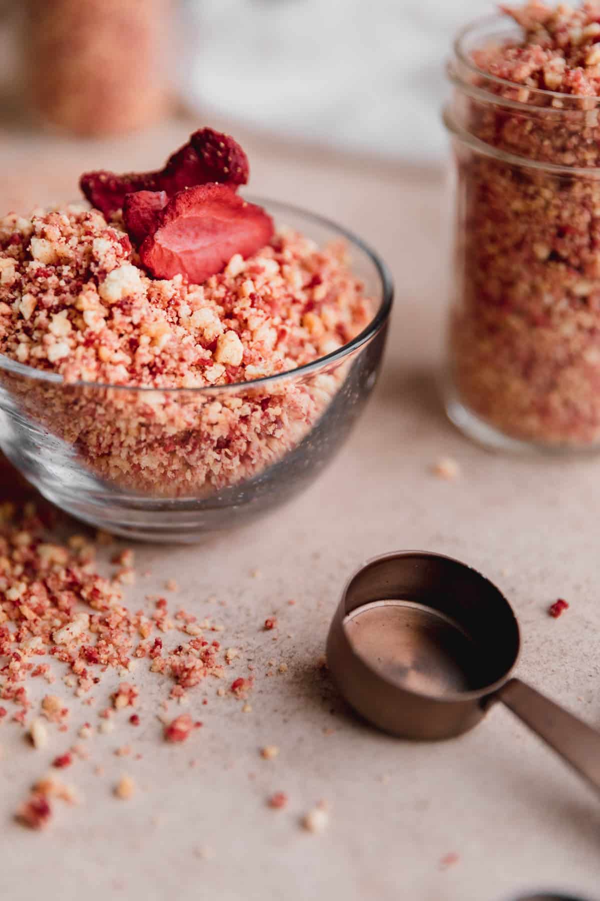 Strawberry Crunch Crumble in a small clear bowl with a measuring spoon to the side. 