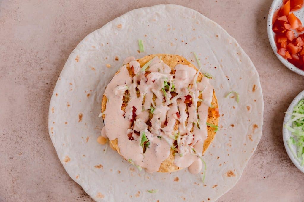 A tostada, lettuce, tomato, Tajin, Cholula and taco ranch on top of the ground beef. 