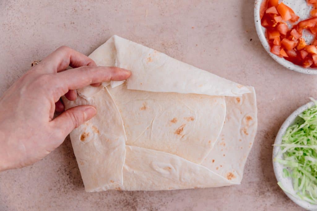 Large flour tortilla being folded up around the tostada. 