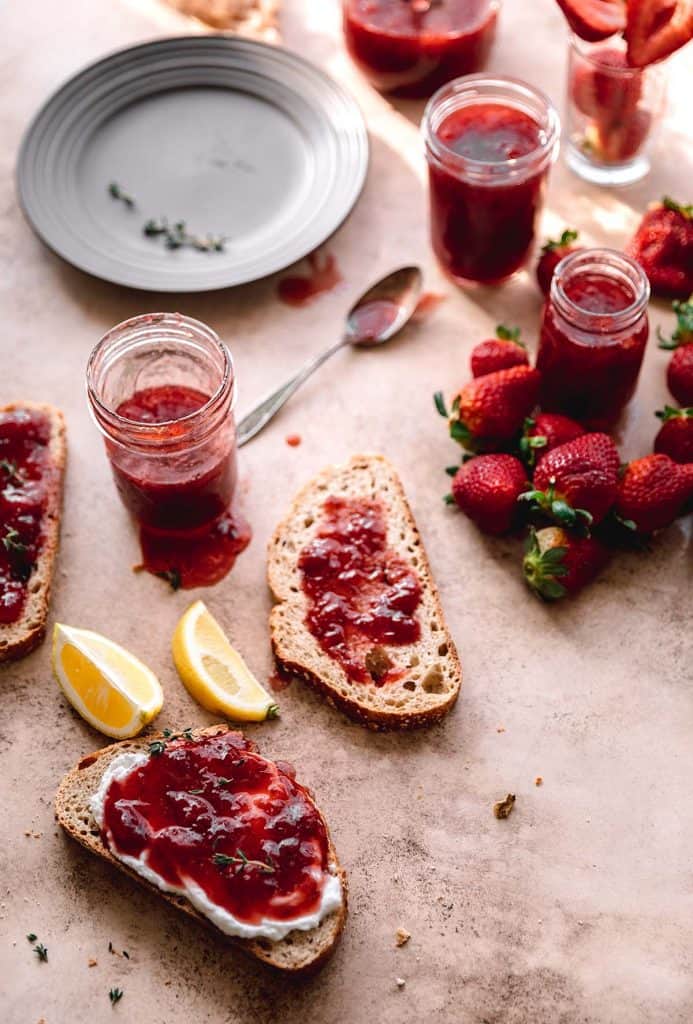 strawberry jam in multiple jars and spread on toast with plates and lemon wedges