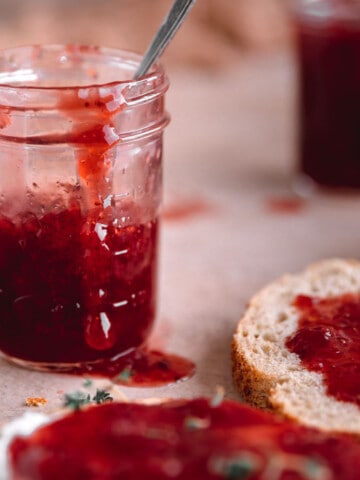 The Best Strawberry Jam in a glass jar with a drop running down the side.