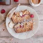 Two slices of Honey Almond Banana Bread with raspberry on a plate topped with powdered sugar.