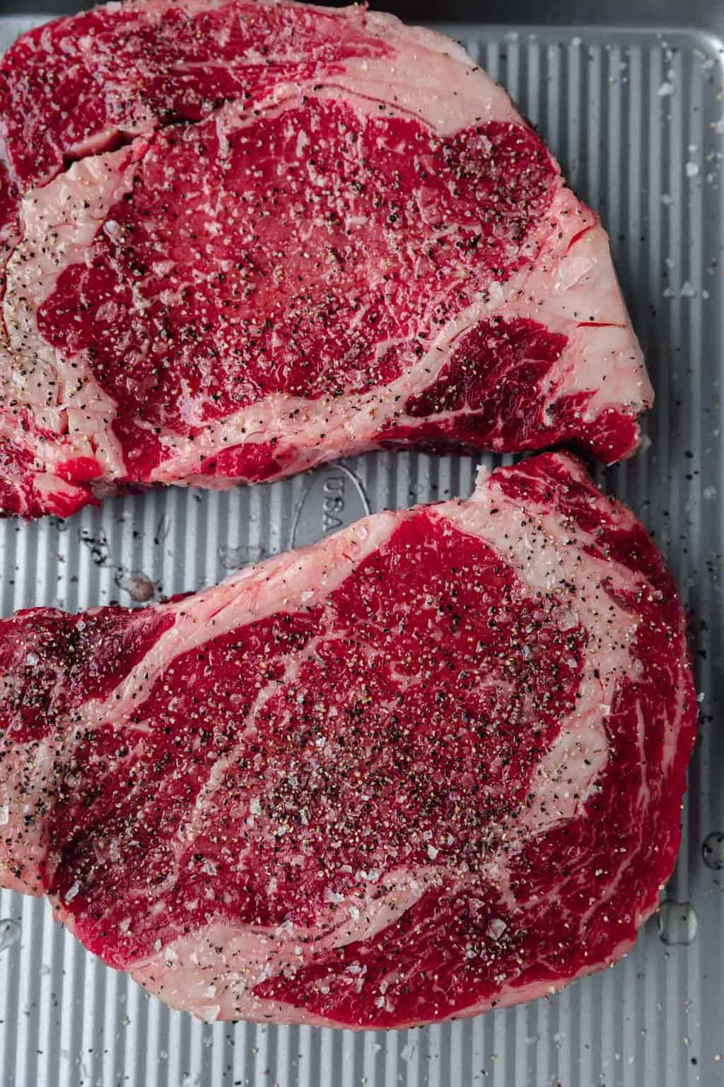 raw ribeye steaks seasoned with salt and pepper