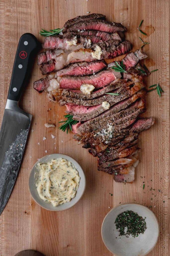 ribeye steak sliced on the cutting board with a knife next to it and butter on top