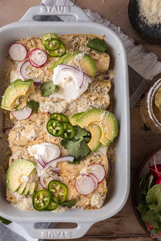 creamy green chile chicken enchiladas topped with sour cream, jalapeno, avocado and radish