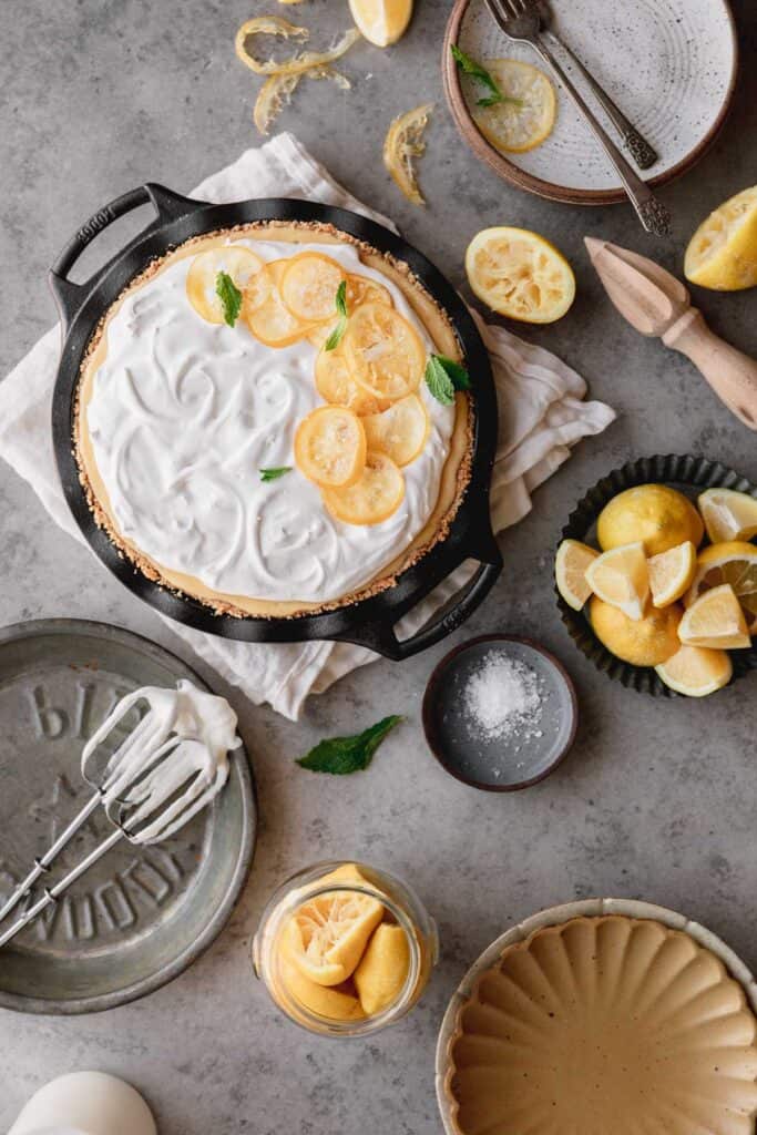 over head shot of the creamy lemon pie with candied lemons, lemon wedges and utensils used to make it