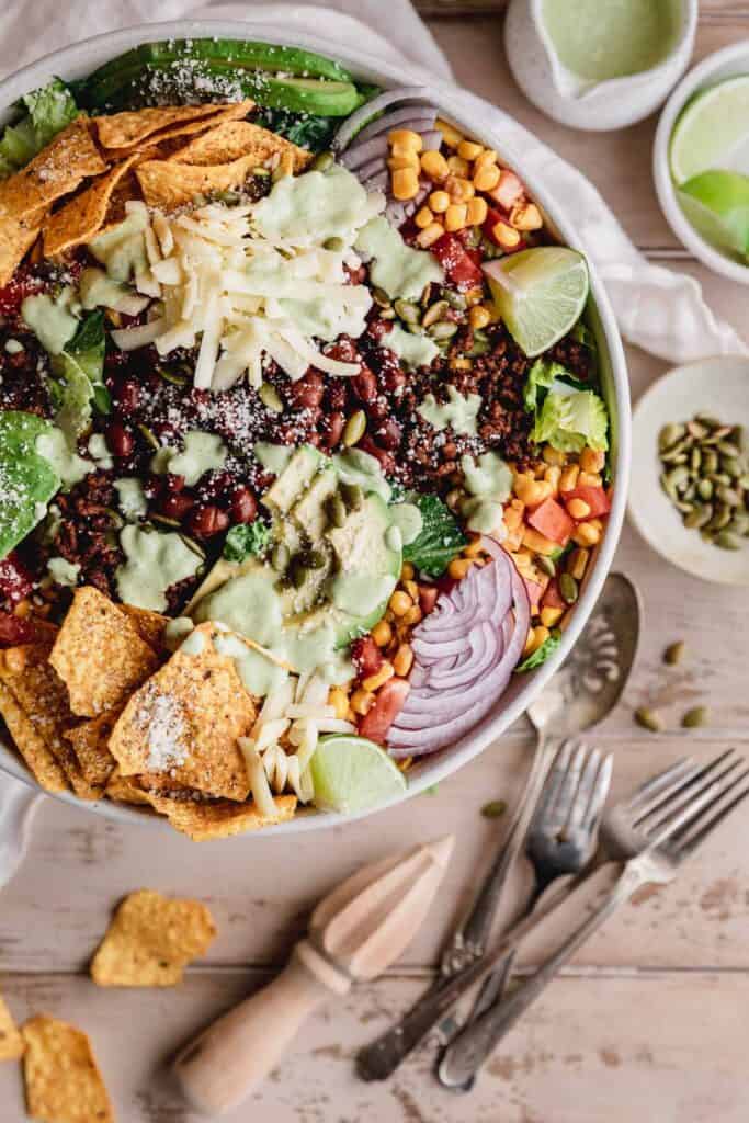 a large bowl of Dorito taco salad with silverware and ingredients off to the right side