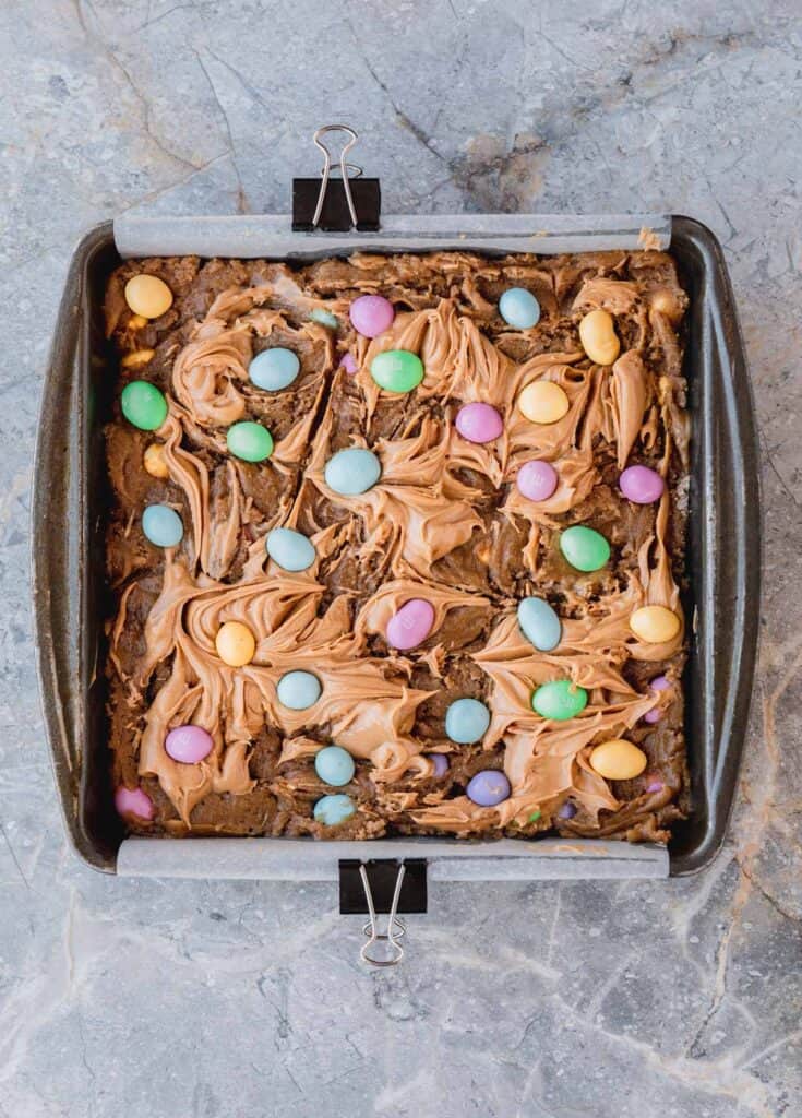 Easter peanut butter blondie batter spread into a pan, swirled with peanut butter then topped with M&M's