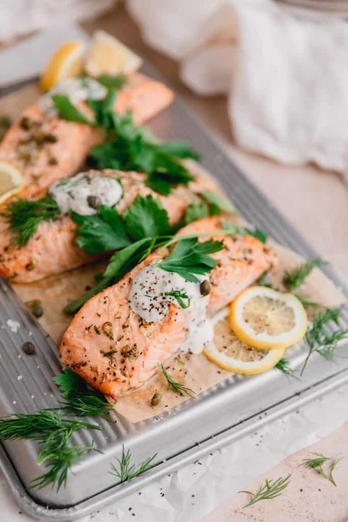 the perfect air fryer salmon on a tray with tartar sauce, herbs and lemon