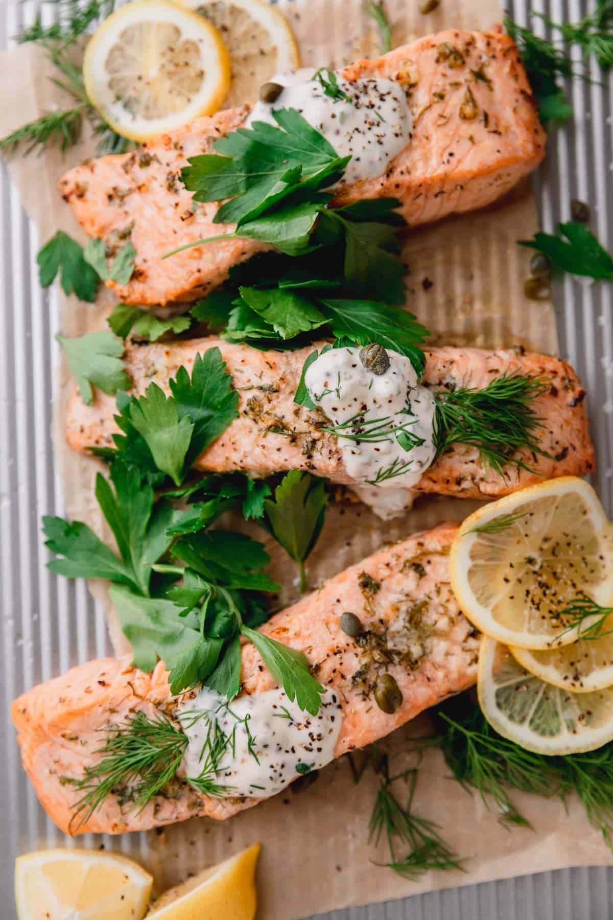 Air Fryer Salmon recipe with homemade tartar sauce, fresh parsley and lemons on a sheet tray.