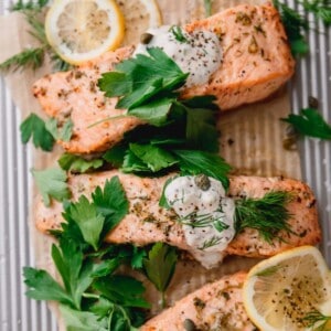 The perfect air fryer salmon recipe topped with homemade tartar sauce, fresh parsley and fresh lemon on a sheet tray.