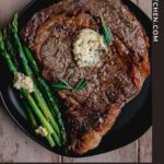 ribeye steak on a black plate topped with herbed butter alongside air fried asparagus
