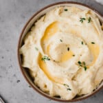 A bowl of Boursin Mashed Potatoes topped with melted butter and fresh thyme.