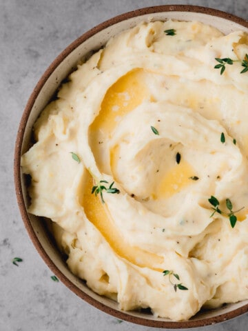 A bowl of Boursin Mashed Potatoes topped with melted butter and fresh thyme.