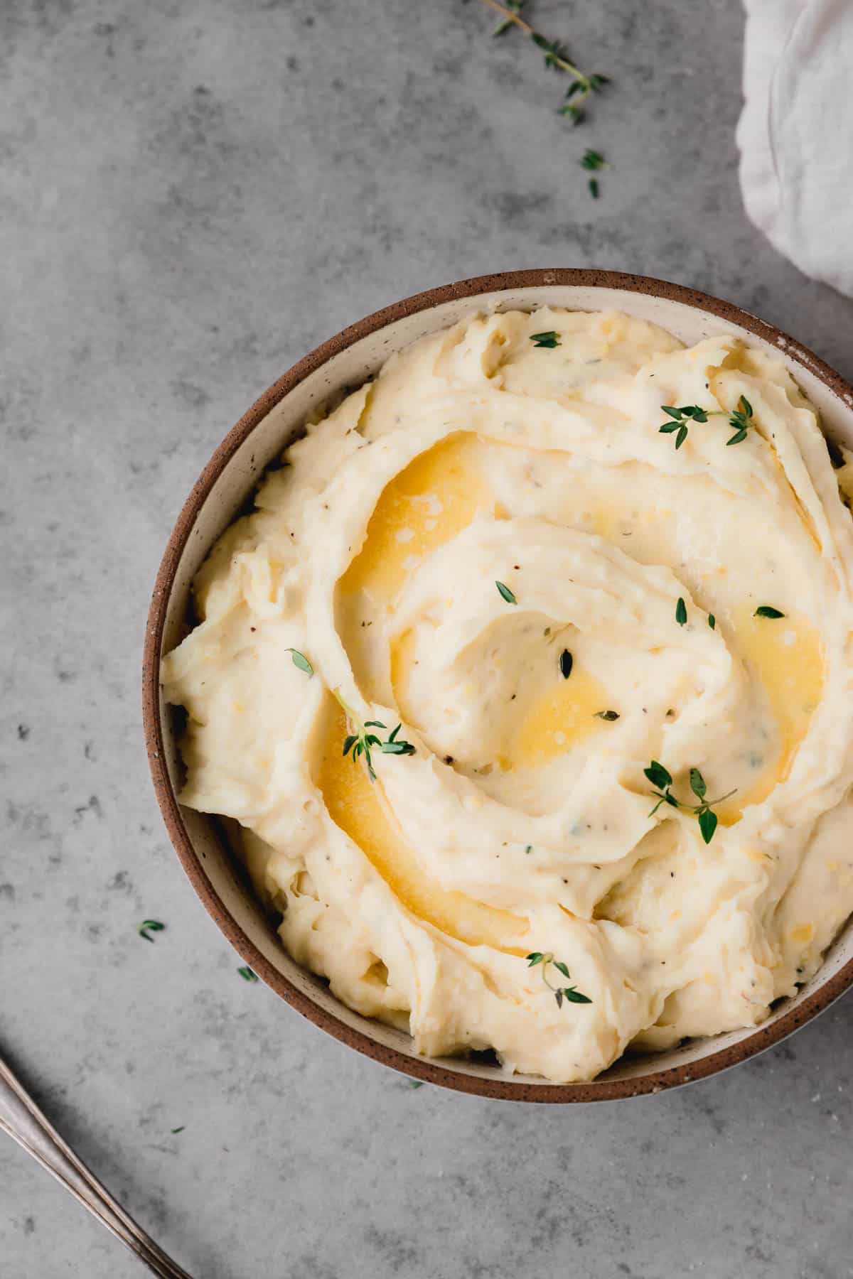 A bowl of Boursin Mashed Potatoes with fresh thyme and butter on top.