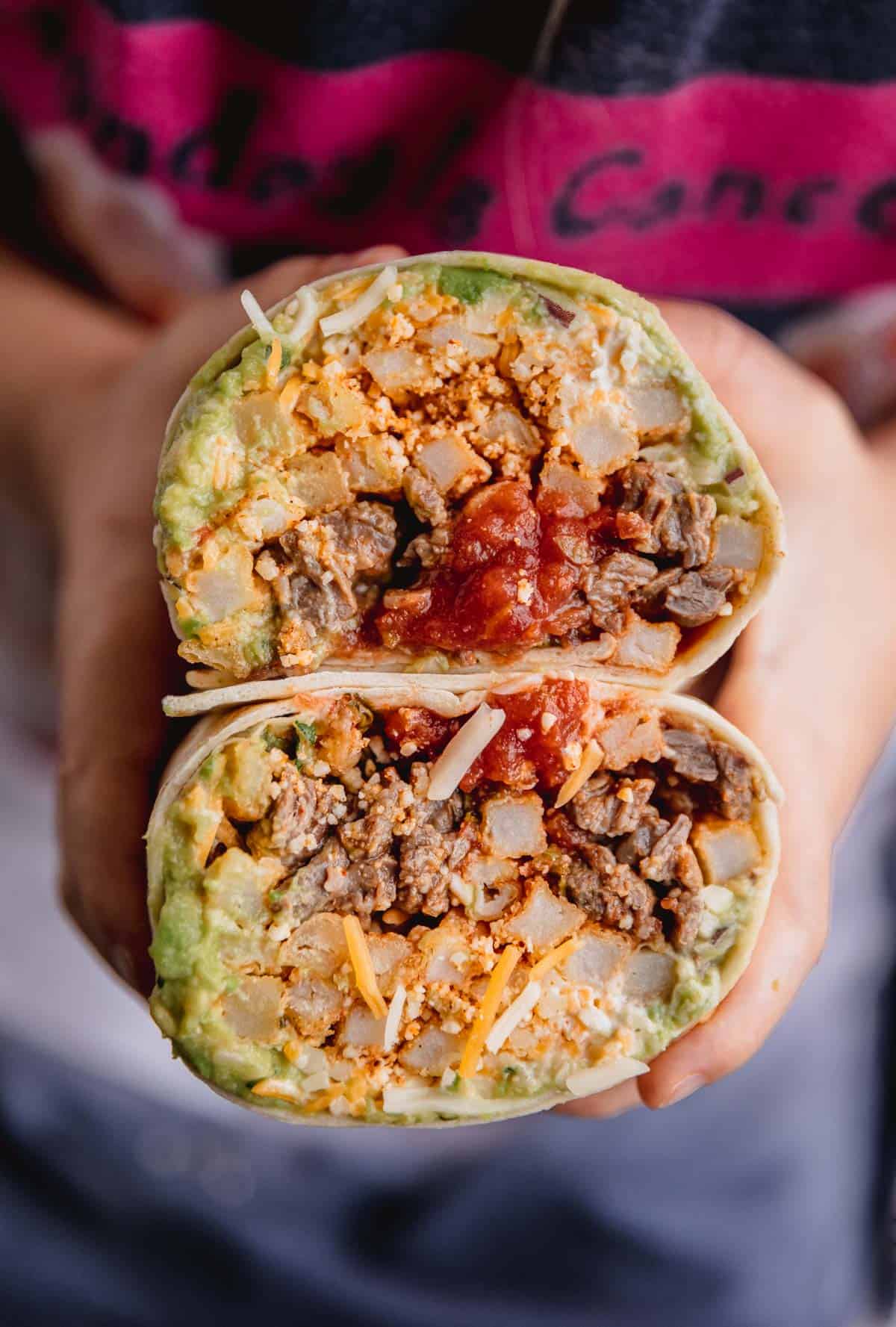 California Burrito cut in half and folded on top of each other while someone holds it.