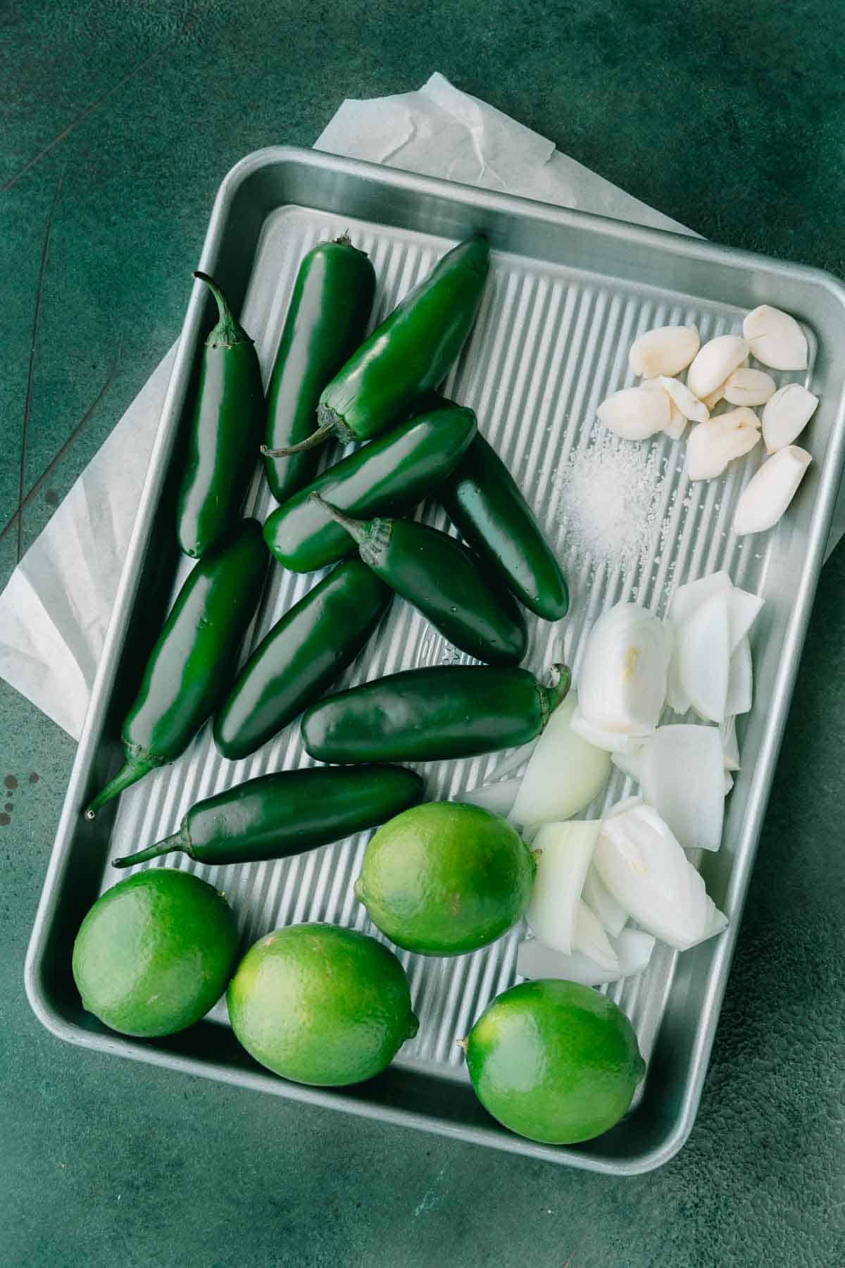 Jalapenos, onions, garlic, salt and limes on a sheet pan. 