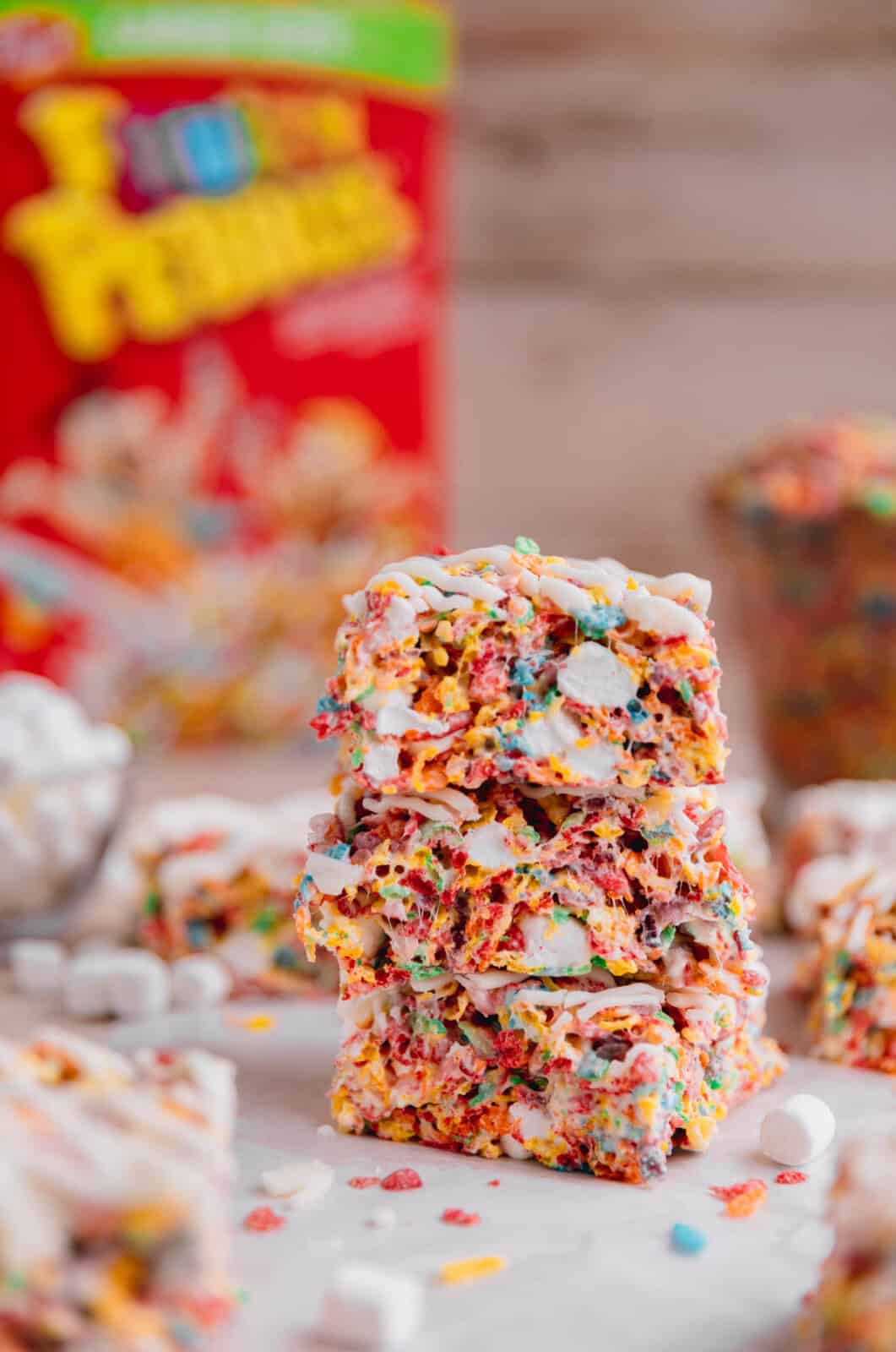 A stack of fruity pebble rice crispy treats with a cereal box in the background.