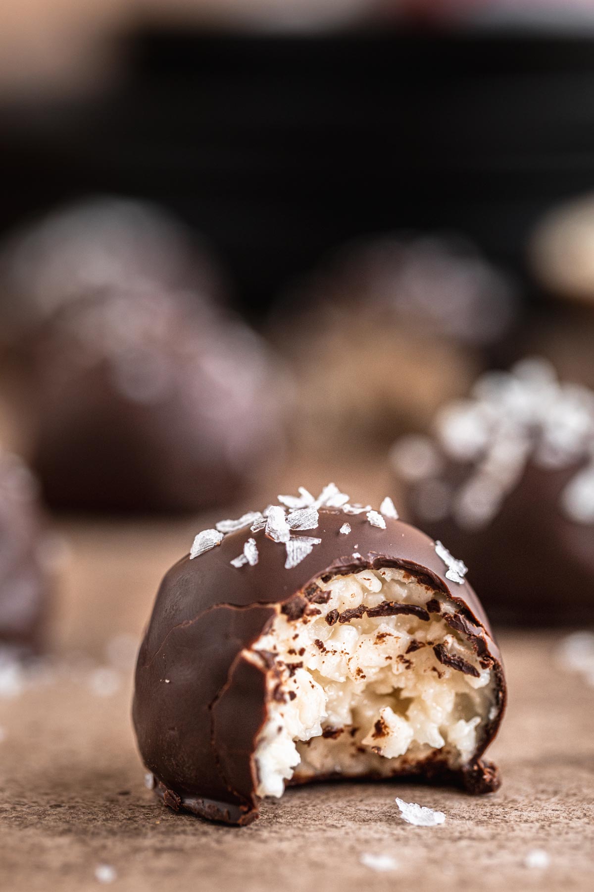 Easy no bake Chocolate Coconut Balls topped with flaky sea salt and has a bite taken out. 