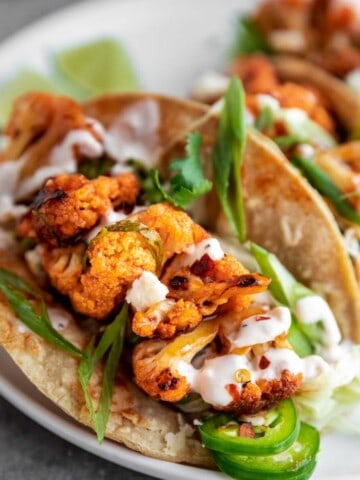 Buffalo Cauliflower Tacos on corn tortillas with green onion, white sauce and jalapenos.
