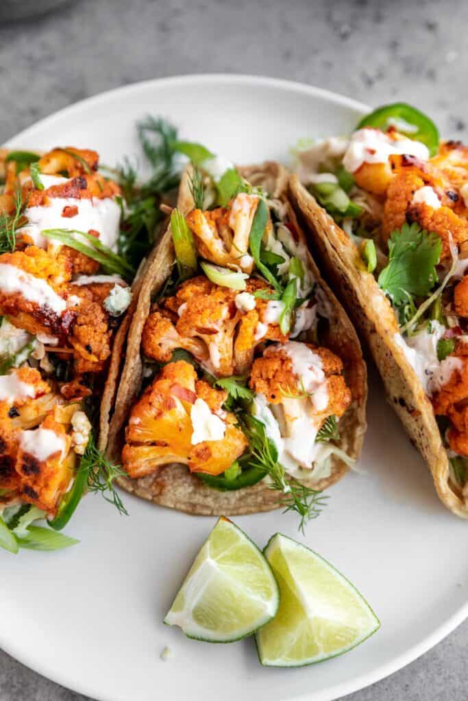 three of the best buffalo cauliflower tacos on a plate with lime wedges 