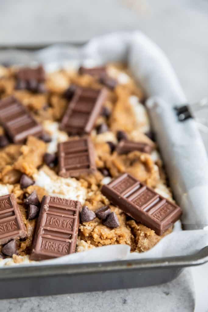 s'mores cookie bars in a pan topped with Hershey's chocolate before being baked 