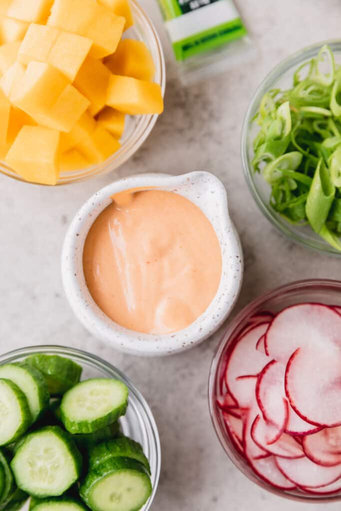 Spicy mayo in a white dish surrounded by fresh fruits and veggies.