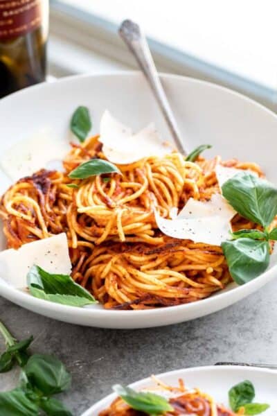 A bowl of spaghetti with basil, parmesan and a bottle of wine.