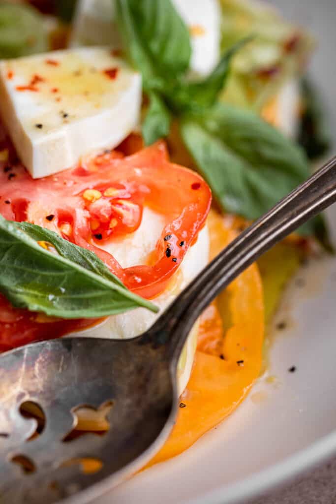 close up of the tomatoes, basil, mozzarella and dressing in a bowl with a spoon