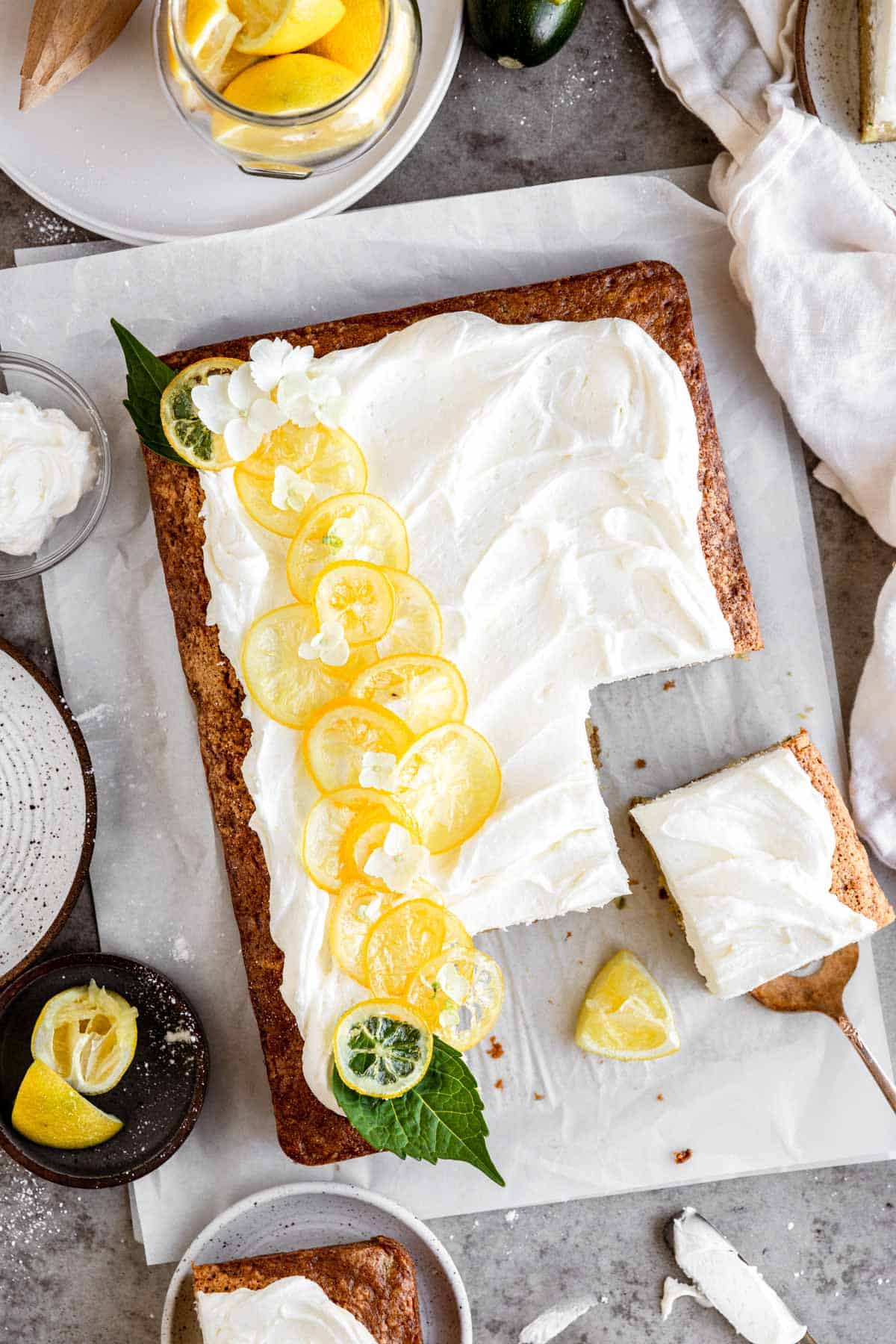 Lemon Zucchini Cake with lemon cream cheese frosting and candied lemons on top that has a few slices taken out. 