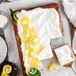 lemon zucchini cake with lemon buttercream frosting topped with candied lemons. cake has a couple slices cut out