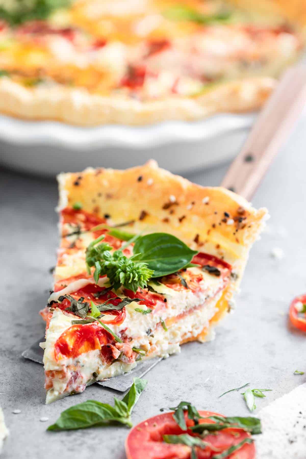 A slice of Tomato Pie with basil leaves on top.