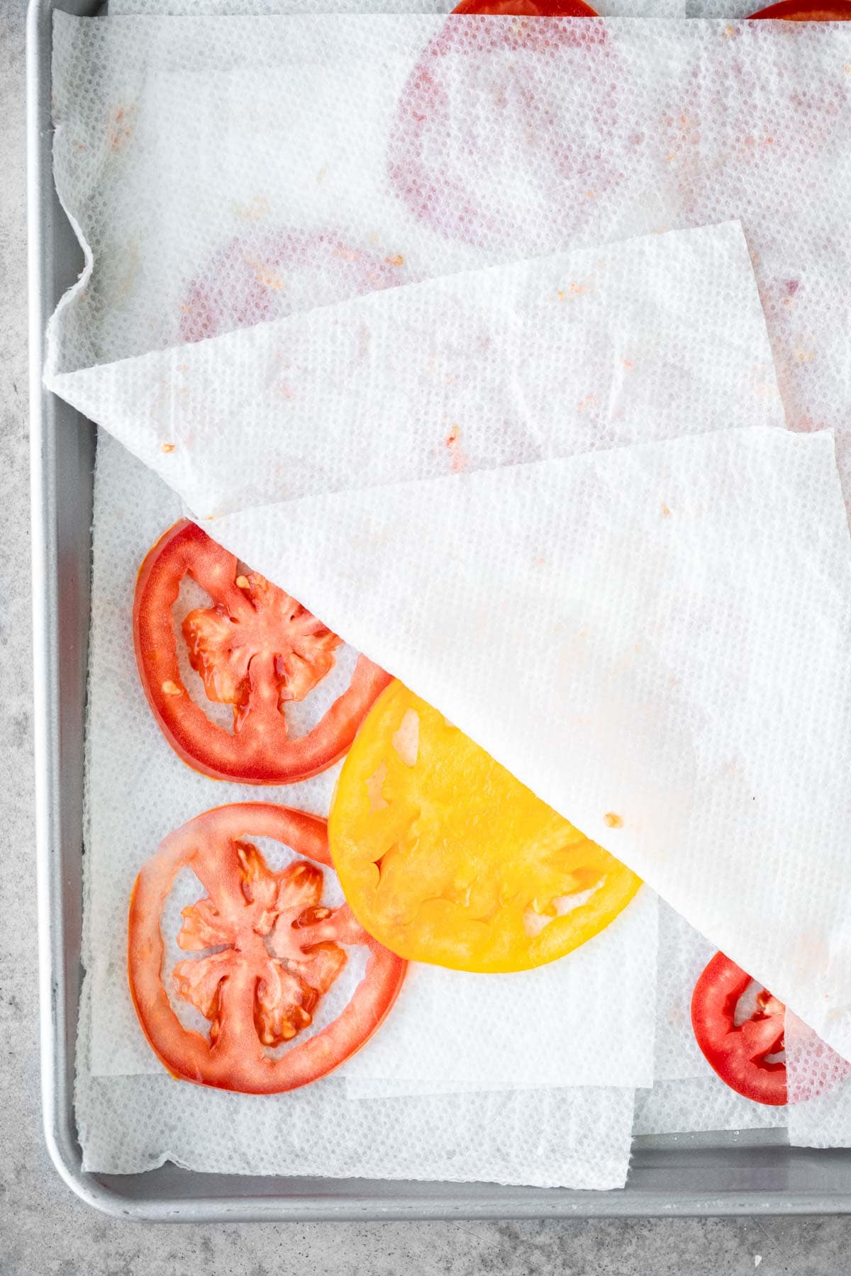 Tomatoes on a sheet tray with paper towels under and over them, drying them out.