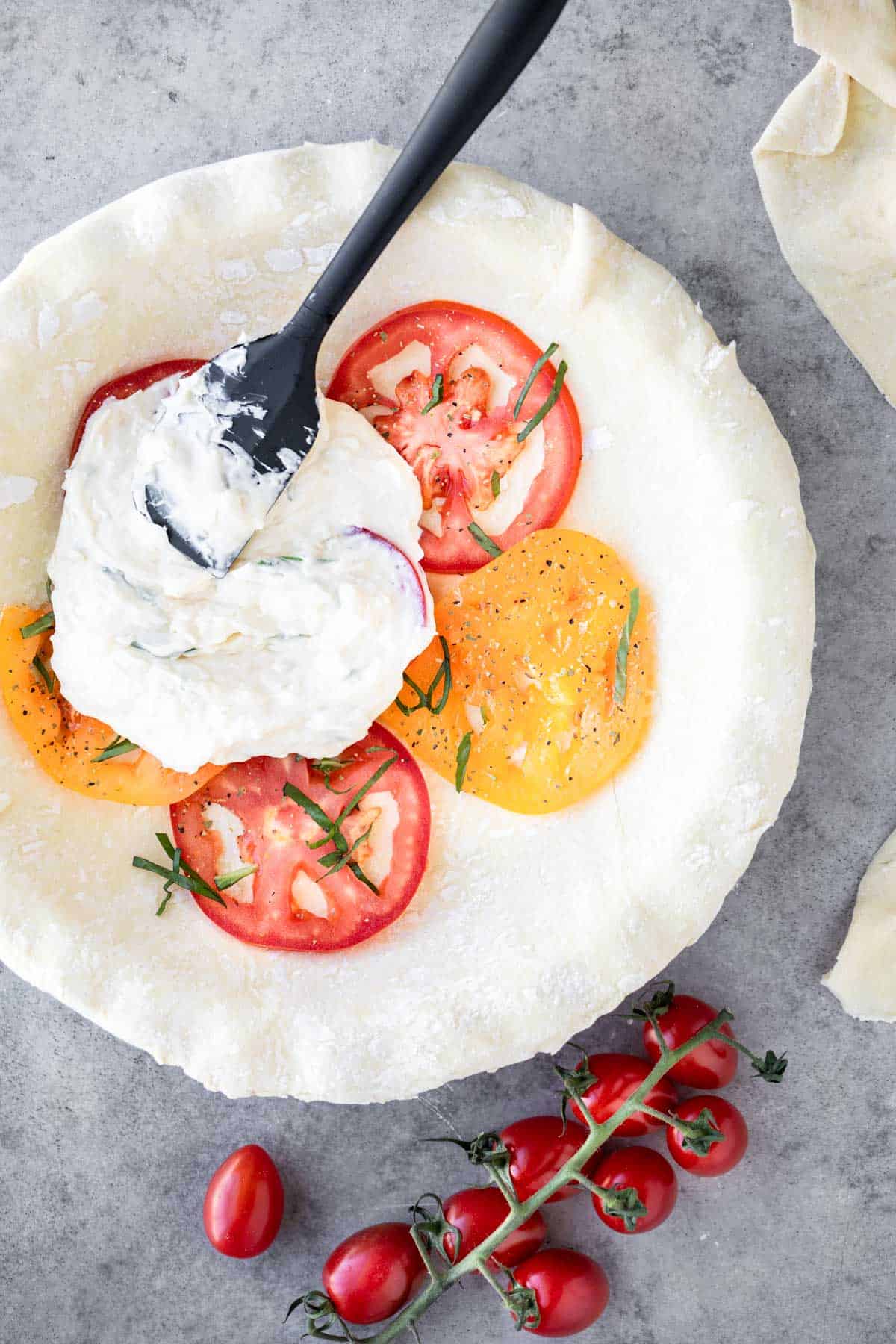 Tomatoes and cheese in the bottom of a raw pie crust with a spatula on top.