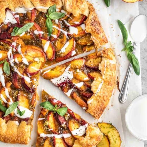 A spicy peach galette topped with goat cheese drizzle with one slice cut out of it. A serrano pepper, half a peach and bowl of sauce next to it.