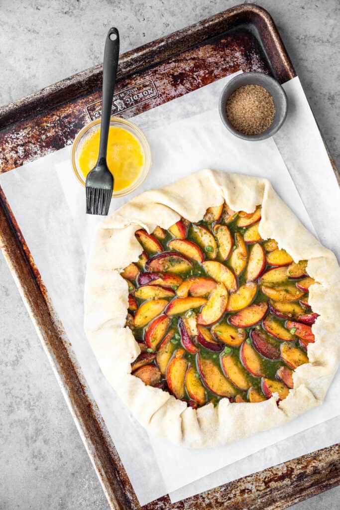 Spicy peach galette on a baking sheet with egg wash, ready to go in the oven. 