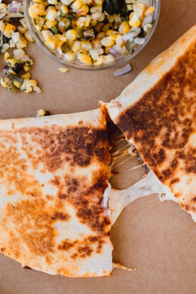 a cheese pull between pieces of the quesadilla with corn salsa to the side