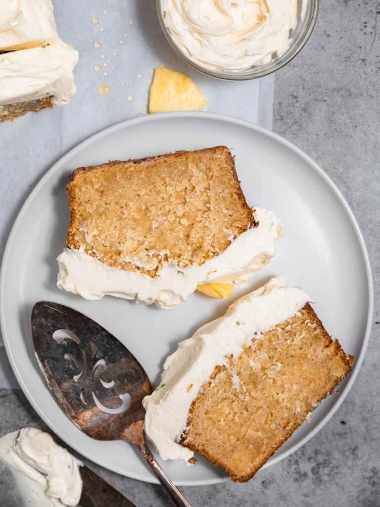 Two slices of cake on a plate that have been topped with honey buttercream frosting and have a serving spatula next to them.