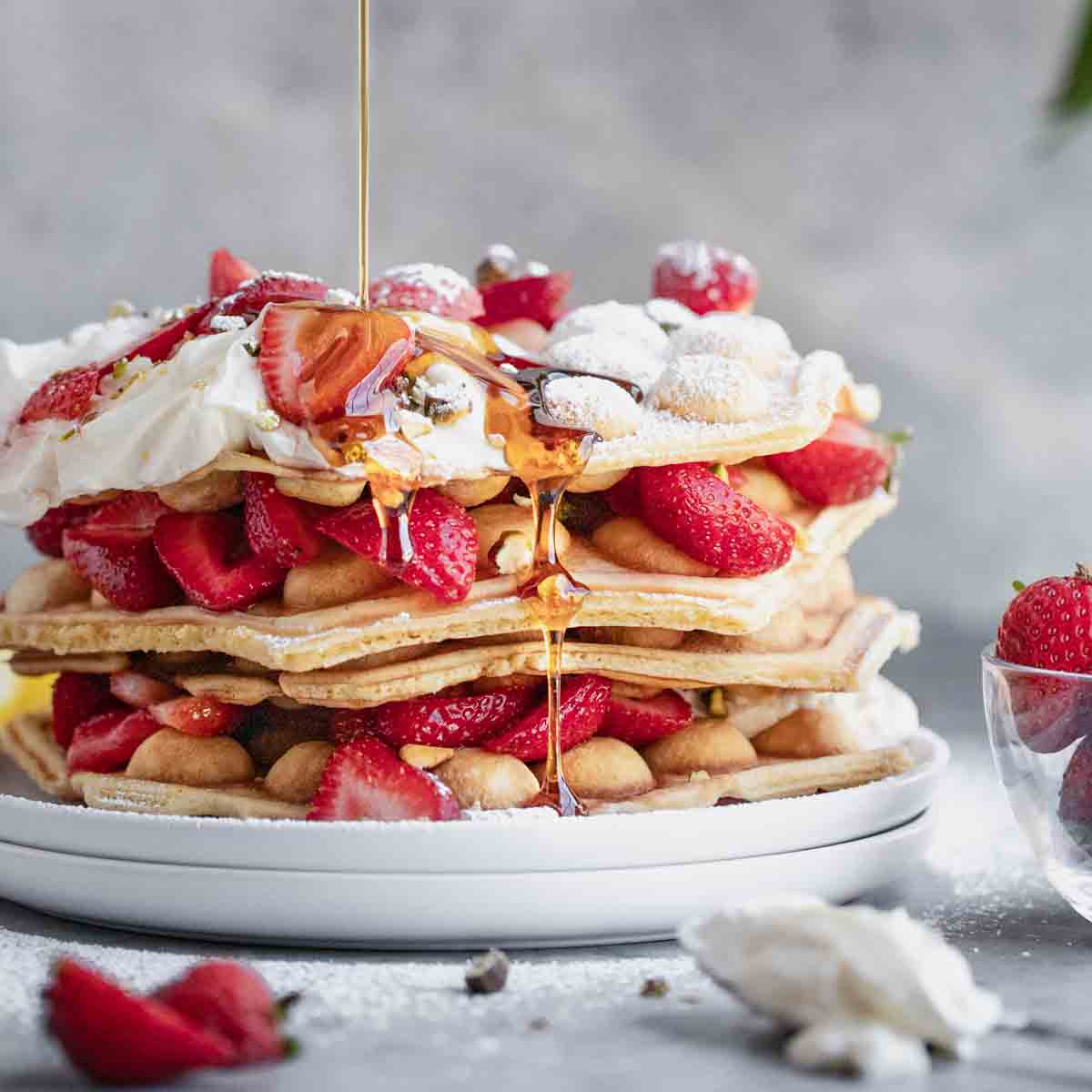 Bubble Waffles stacked with strawberries, cream, pistachios and syrup.