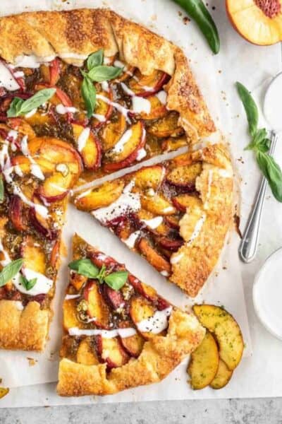 A spicy peach galette topped with goat cheese drizzle with one slice cut out of it. A serrano pepper, half a peach and bowl of sauce next to it.