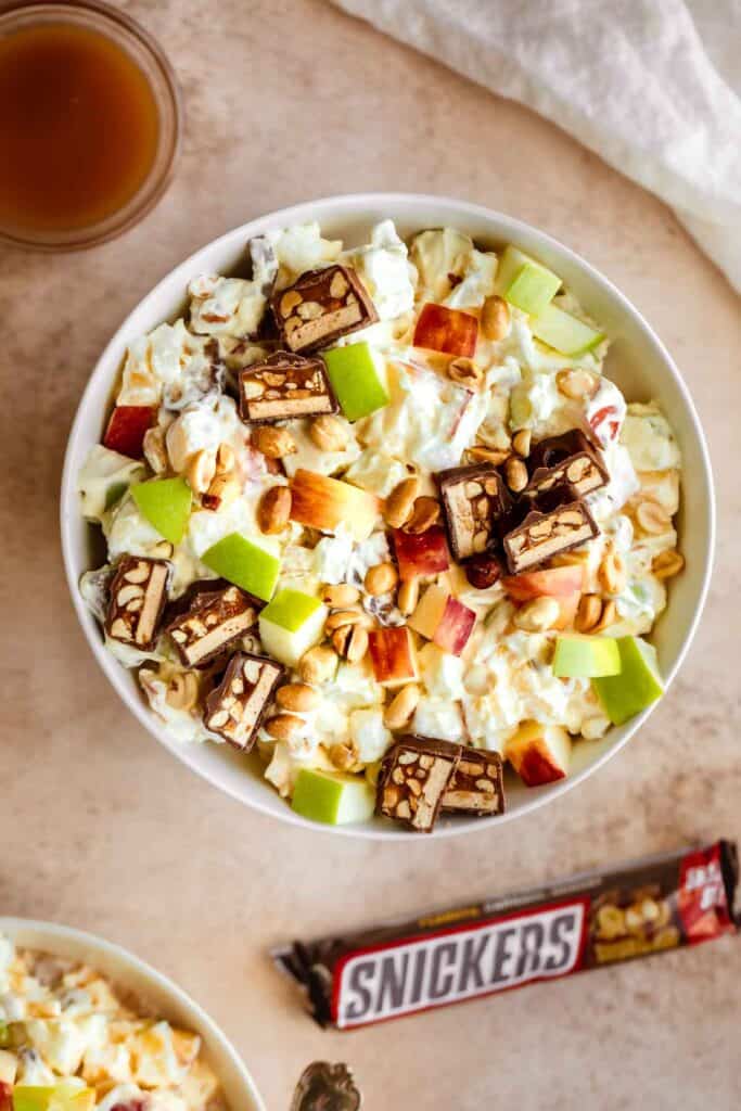 A bowl of Taffy Apple Salad with Snickers in it, a Snickers bar to the side and a dish of caramel