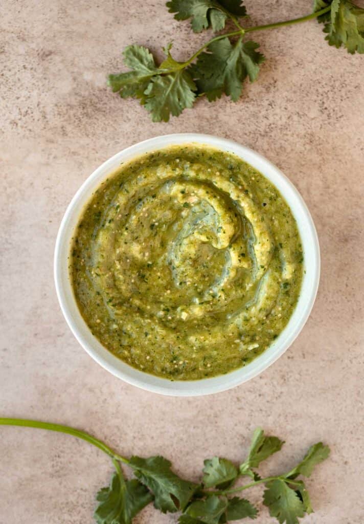 Salsa verde in a white bowl with stalks of cilantro to the top and bottom of the bowl.